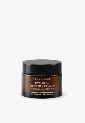 Hyaluronic acid cream in a dark amber jar with a black lid. Label features white text detailing product and ingredients.