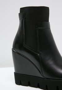 Botín de tobillo negro con superficie de cuero suave, panel elástico y suela texturizada. Presenta una silueta elegante y un diseño minimalista.