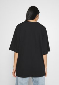 Svart oversized t-skjorte med korte ermer, laget av bomull, rund hals og en jevn tekstur. Baksiden har et enkelt design uten trykk.