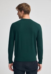 Grüner Pullover mit langen Ärmeln und rundem Ausschnitt, aus einem glatten, weichen Stoff gefertigt, mit einem taillierten Bund und Ärmelsäumen.