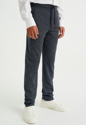 Marineblå joggebukser med tekstur, elastisk taljebånd, snørejustering og sidelommer, kombineret med hvide sneakers.