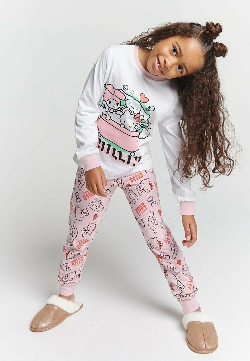 White long-sleeve pajama top with pink accents and cartoon graphic. Pink pajamas with a repeating Hello Kitty pattern. Tan slippers with white lining.