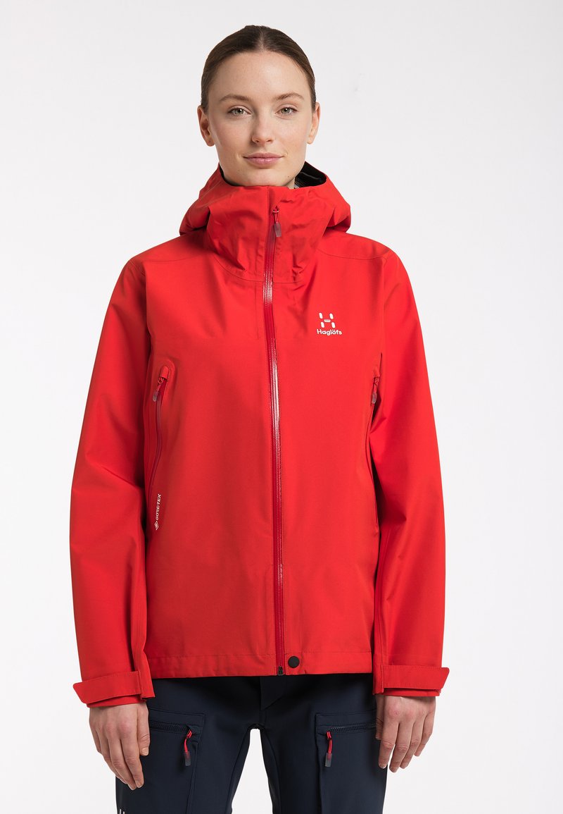 Červená voděodolná bunda s plným zipem, nastavovací kapucí a kapsami na zip. Má elastické manžety a logo na hrudi. Hedvábná textura.