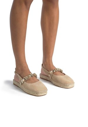 Espadrilles en suède beige avec une sangle décorative arborant un accent en perles, un bout rond et une semelle en jute tressé. Le design comprend des côtés découpés.