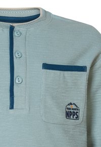 Hellblaues, strukturiertes Hemd mit Rundhals, zwei Knöpfen und einer Brusttasche, die ein Berglogo in Dunkelblau und orangefarbigen Akzenten zeigt.
