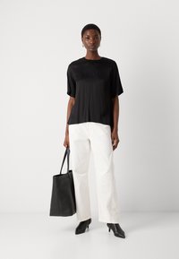 Svart kortermet satengbluse med rund hals, kombinert med høy midje hvite vide bukser og en svart totebag.