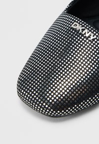 Černá dámská balerína s perforovaným vzorem, hladkým povrchem a stříbrným logem DKNY na svršku. Špičatý tvar špičky pro elegantní vzhled.