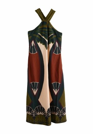 Femme portant une robe longue sans manches avec des motifs géométriques et en forme d’éventail en vert, marron, noir et crème, debout sur une terrasse en bois.