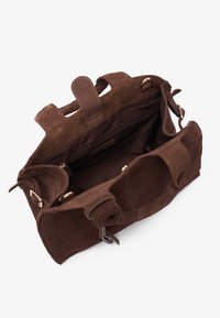 Bruine suède handtas met een ritsvak aan de binnenkant, korte handvatten en gespsieraden, gekenmerkt door een zachte textuur en een open ontwerp.