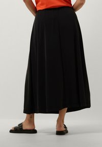 Sort midi-nederdel med en glat tekstur, elastisk talje og en afslappet pasform. Kombineret med sorte slidesandal.