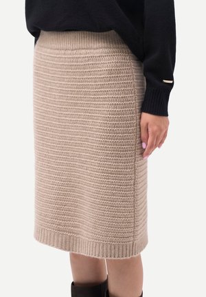 Beiger, gestrickter Rock in knieumspielender Länge, getragen mit schwarzem Pullover und Stiefeln, Seitenansicht mit geripptem Bund und Saum.