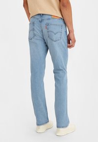 Light blue denim jeans with straight legs, subtle fading, and two back pockets featuring a signature stitched design.
