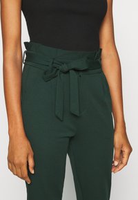 Gröna byxor med bälte gjorda av mjukt tyg, med knytmidja, sidofickor och en skräddarsydd passform för en strukturerad look.