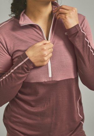 Person zipping up a two-tone maroon and pink long-sleeve athletic top with contrasting white zipper and seam details.