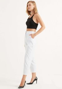 Zwarte cropped tanktop, witte pinstriped tapered broek met zakken en zwarte puntige hakken. Glad materiaal met een slim fit.