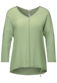 Light green long-sleeve top with a V-neck, featuring a straight cut, smooth texture, and adjustable drawstring detail at the hem.