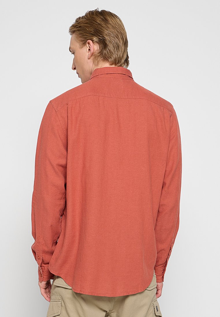 Chemise à manches longues en tissu brun-rouge, dotée d'un col, de poignets boutonnés et d'une coupe droite avec un ourlet arrondi à l'arrière.