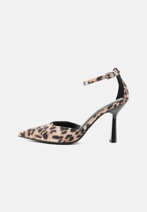 Escarpin à bout pointu avec imprimé léopard, bride de cheville avec boucle et talon noir fin sur fond blanc.