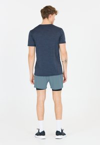 Kurzärmliges, dunkelblaues Sportshirt mit strukturierter Oberfläche, kombiniert mit hellblauen Shorts. Modell trägt weiße Socken und dunkle Sneakers.