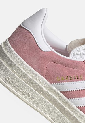 Różowe zamszowe i białe skórzane buty sportowe Adidas Gazelle z teksturowaną kremowo-białą podeszwą i złotym napisem "GAZELLE" po boku.