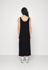 Svart ärmlös maxiklänning med djup rygg, tillverkad av lättviktig tyg. Buren med silverfärgade sneakers och vita strumpor.