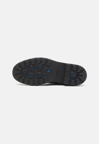 Semelle de chaussure noire en matériau en caoutchouc flexible, dotée de six trous de ventilation circulaires et d'un profil texturé pour une bonne adhérence.