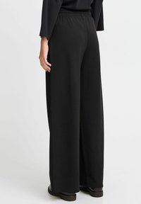 Schwarze weite Hose mit elastischem Bund, glatter Stoffoberfläche und lockerer Passform. Akzentuiert durch minimale Nähte.