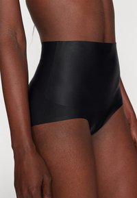 Shapewear noir taille haute fabriqué à partir d'un tissu lisse, avec un design élégant et des bords sans couture pour un confort optimal.