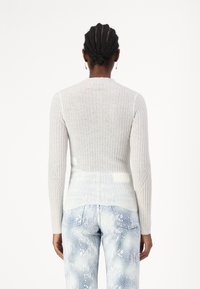 Lys grå ribbestrikket genser med lange ermer, med høy hals og kontrasterende hvite paneler bak. Kombinert med blå jeans med slangemønster.