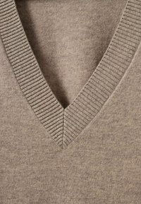 Pulover cu decolteu în V de culoare maro deschis, realizat dintr-un material moale. Are o textură ribaltă la guler și o textură generală netedă.