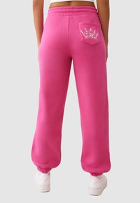 Roze joggingbroek met een ontspannen pasvorm, elastische tailleband en enkelschoenen. Voorzien van een achterzak met een kroonontwerp in rhinestones.