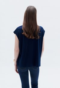 Top blu navy a maniche corte dal taglio morbido, realizzato in materiale morbido, con scollatura rotonda e texture liscia, abbinato a jeans blu scuro.