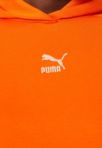 Heldere oranje hoodie met een klein wit Puma-logo en een springende kat boven de merknaam op de borst.