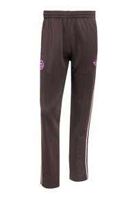 Pantalon de survêtement marron avec taille élastique, logo Adidas rose clair sur la cuisse droite, patch circulaire sur la cuisse gauche et bandes latérales beiges.