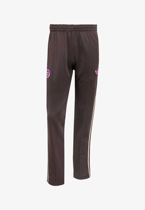 Braune Jogginghose mit elastischem Bund, hellrosa Adidas-Logo am rechten Oberschenkel, rundem Aufnäher am linken Oberschenkel und beigen Seitenstreifen.