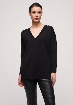 Zwart V-hals gebreid pullover met lange mouwen, zachte textuur en een relaxed-fit, gecombineerd met strakkere zwarte leren broek.
