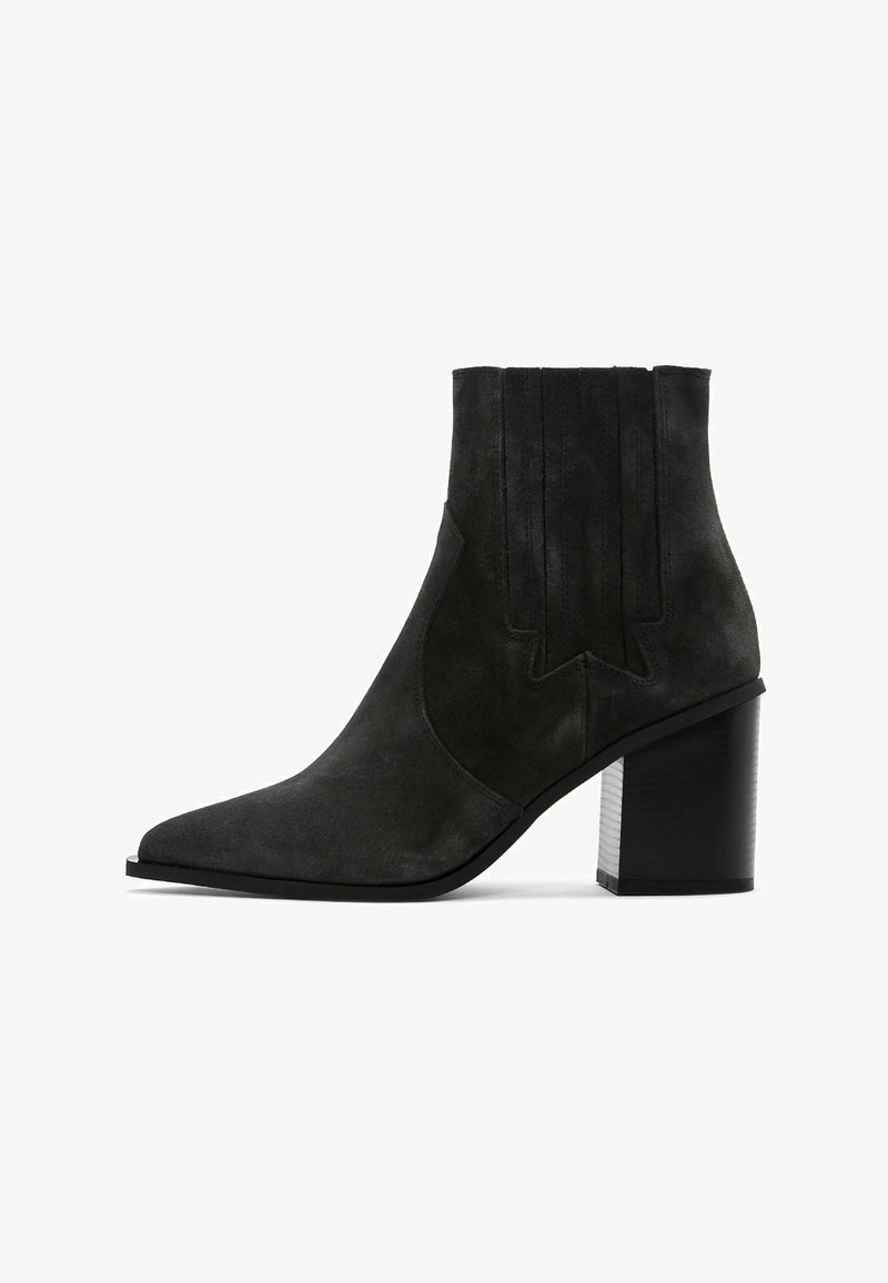 Bottine en suède noir avec un bout pointu, des détails texturés sur les côtés et un talon noir épais. Fini lisse avec des accents minimalistes.