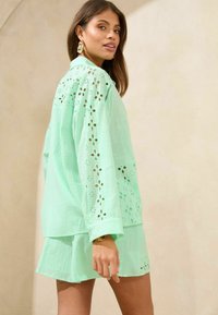 Mintgroene shirt met geborduurde uitsparingen en lange mouwen, gecombineerd met een bijpassende rok. Lichtgewicht stof met een gestructureerde uitstraling.