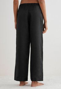 Svarta, vida byxor i mjukt material, med elastiskt midjeband och fållade kanter, designade för komfort och rörelsefrihet.