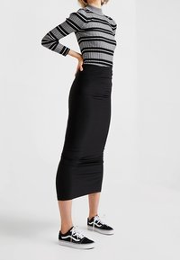 Jupe midi noire associée à un haut ajusté à manches longues rayé gris et noir, complétée par des baskets noires à semelles blanches.