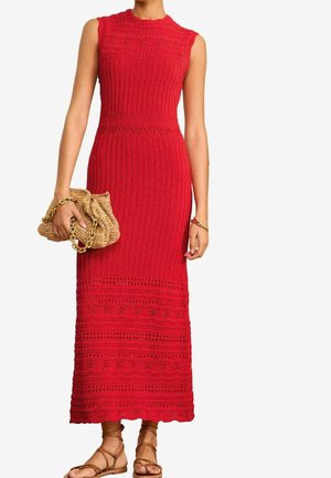Robe midi en maille rouge sans manches avec motifs texturés, portée avec des sandales tressées couleur cuir clair et tenant une pochette tissée couleur cuir clair avec chaîne dorée.