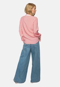 Langärmliges Hemd mit rot-rosa geometrischem Muster; kombiniert mit locker sitzenden, hellblauen Denim-Jeans; entspannter Schnitt; lässiges Design.