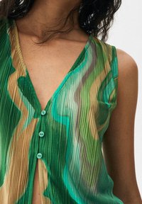 Blusa verde con plisados que presenta un escote en V, cierre de botones con botones azules y un patrón ondulado en tonos variados de verde y marrón.