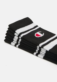 Calcetines negros con rayas blancas y un pequeño emblema rojo, hechos de tela acanalada, apilados en una fila.