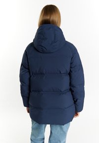Tmavě modrá prošívaná bunda s kapucí, která má prošívaný design a viditelné švy. Spodní lem je vzadu mírně delší.