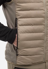 Beige isolierte Weste mit horizontaler Steppung, schwarzen Fleeceärmeln, seitlicher Tasche mit Reißverschluss und verstellbarem Kordelzug in der Taille.