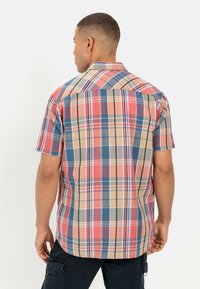 Korte mouw, geruit overhemd in rood, blauw, bruin en cream, met een puntige kraag en een rechte zoom. De stof lijkt lichtgewicht en ademend te zijn.