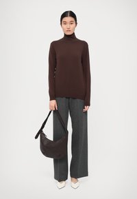 Pull à col roulé marron, pantalon large gris, chaussures pointues blanches et un sac à main tissé foncé avec une bandoulière. Design simple et épuré.