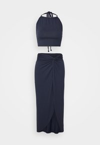 Ensemble deux pièces bleu marine comprenant un haut court à col halter avec des bretelles ajustables et une longue jupe avec un détail torsadé à l'avant.