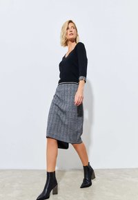 Maglione nero a V con maniche a tre quarti; gonna grigia tessuta con orlo sotto il ginocchio; stivali alla caviglia neri in pelle con tacco a blocco.